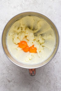 Mixing bowl with creamed butter and sugar, and two egg yolks on top, on a textured surface.