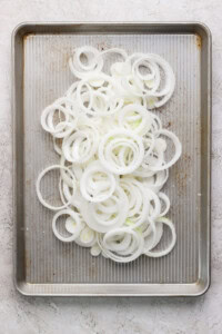 Thinly sliced onion rings spread on a baking sheet with a textured surface.